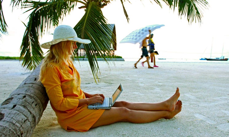 A woman working on a laptop on the beach.