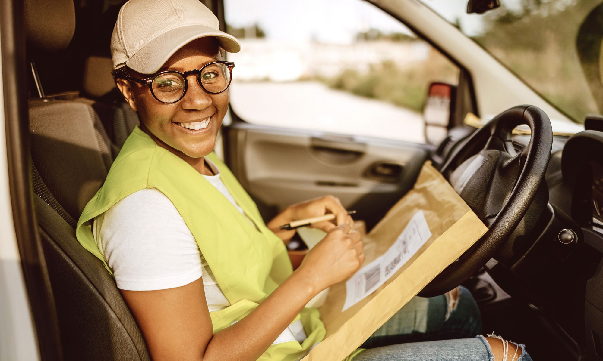Woman holding a parcel while smiling and looking at the camera in the front seat of a van
