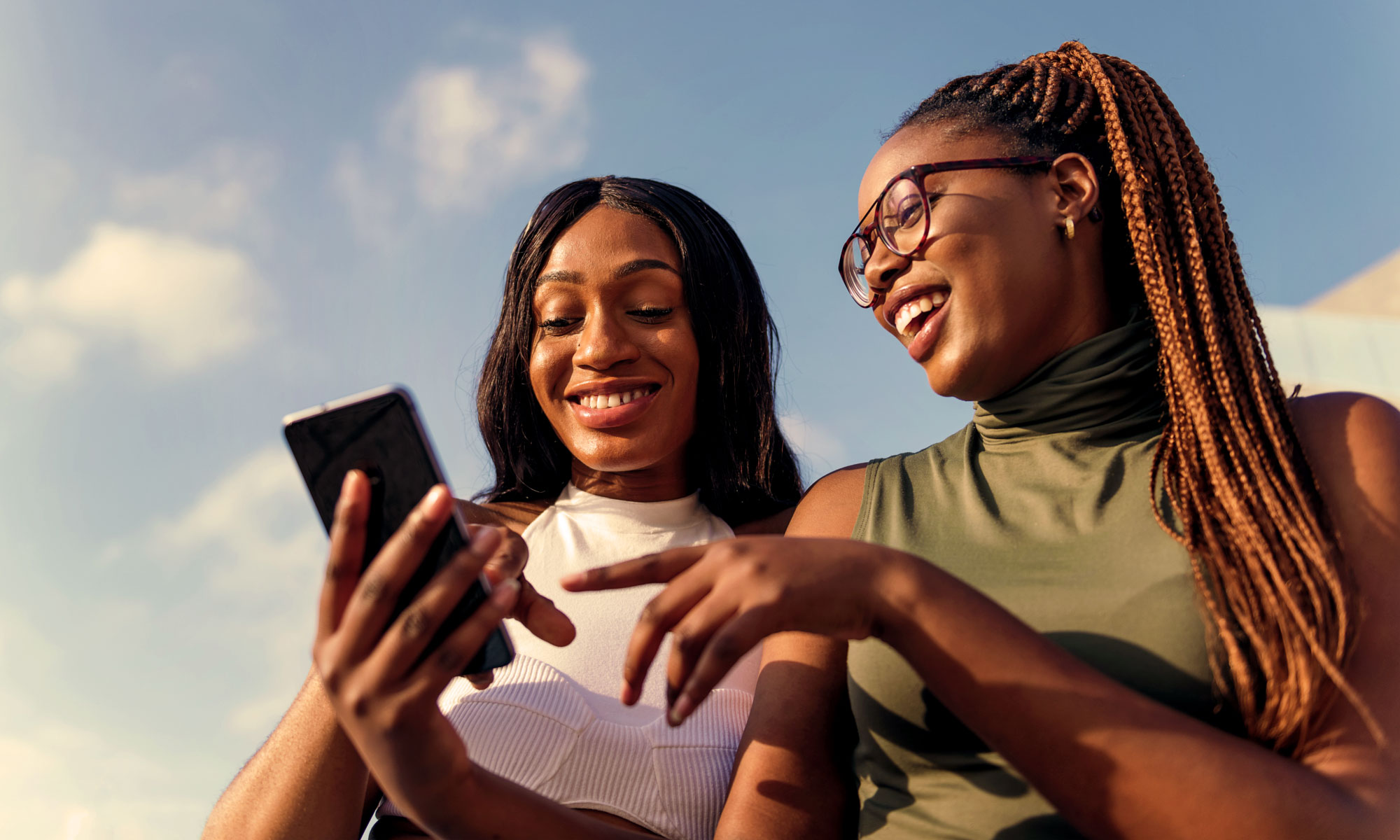 Two young adult women looking at a mobile phone outside