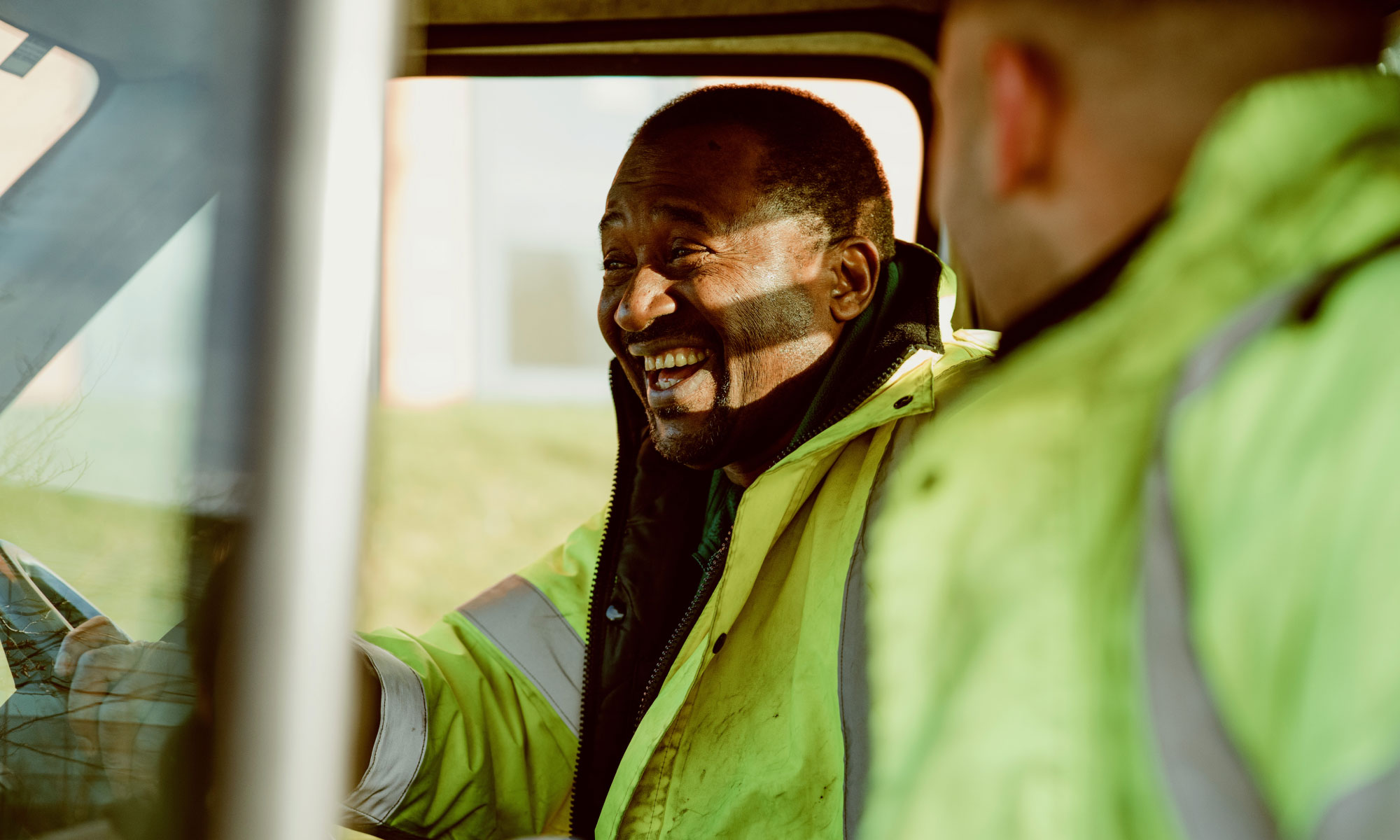 Two van drivers are laughing while wearing high vis vests