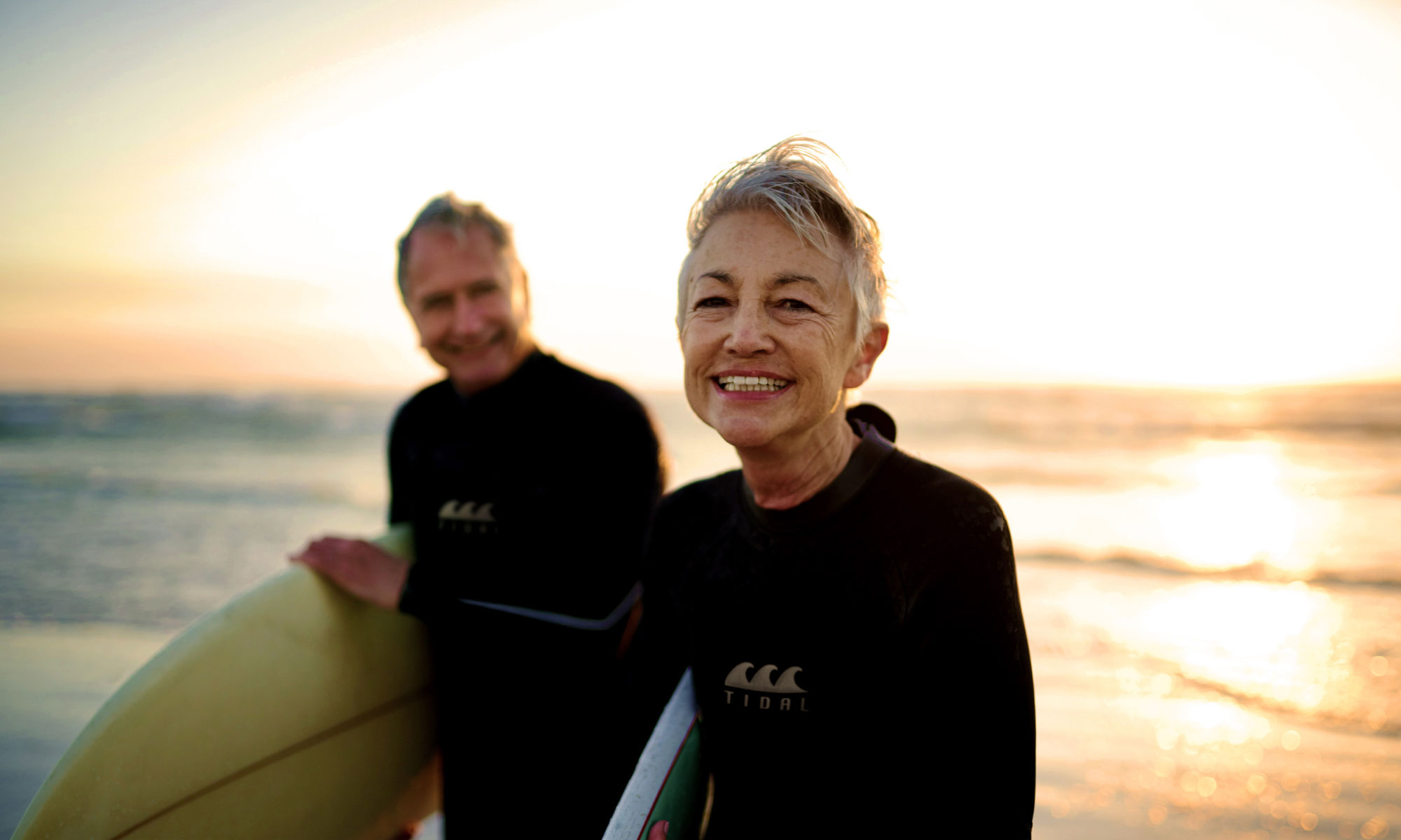 Senior couple wearing wet suits surfing