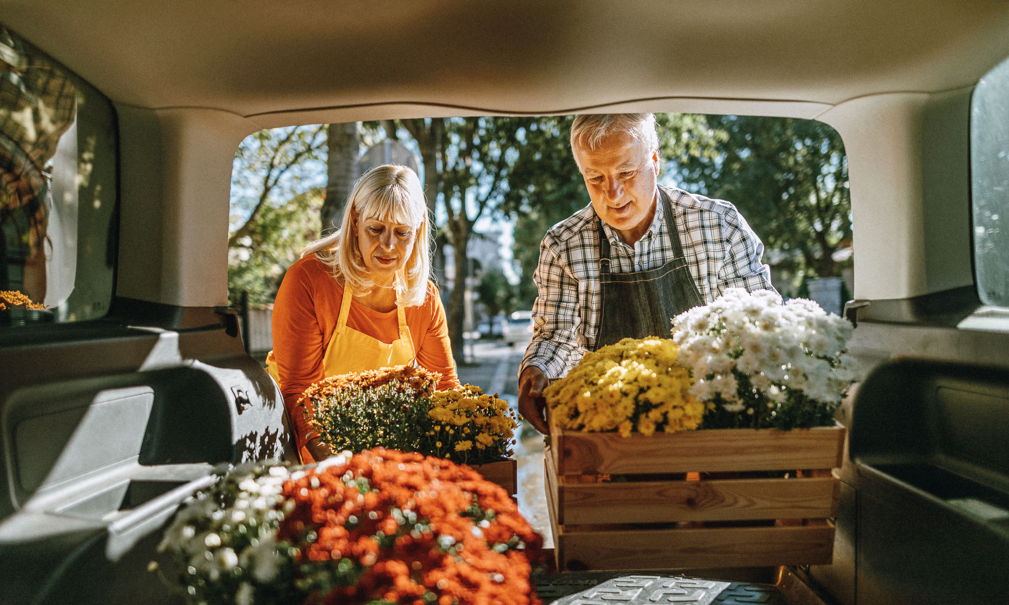 Senior couple loading flowers in the back of their van while wearing aprons