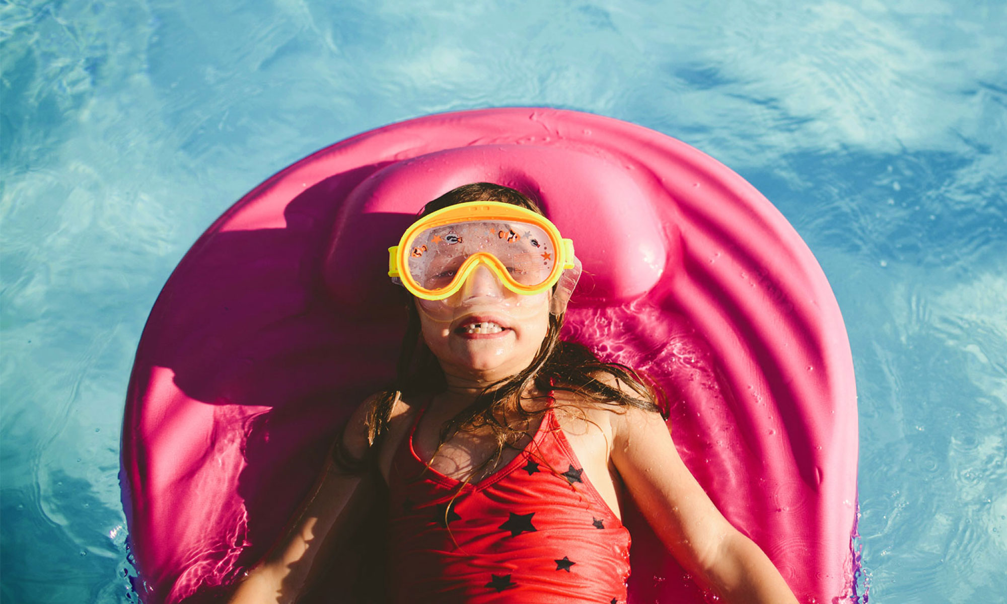 Small girl lying on a pink inflatable in a swimming pool