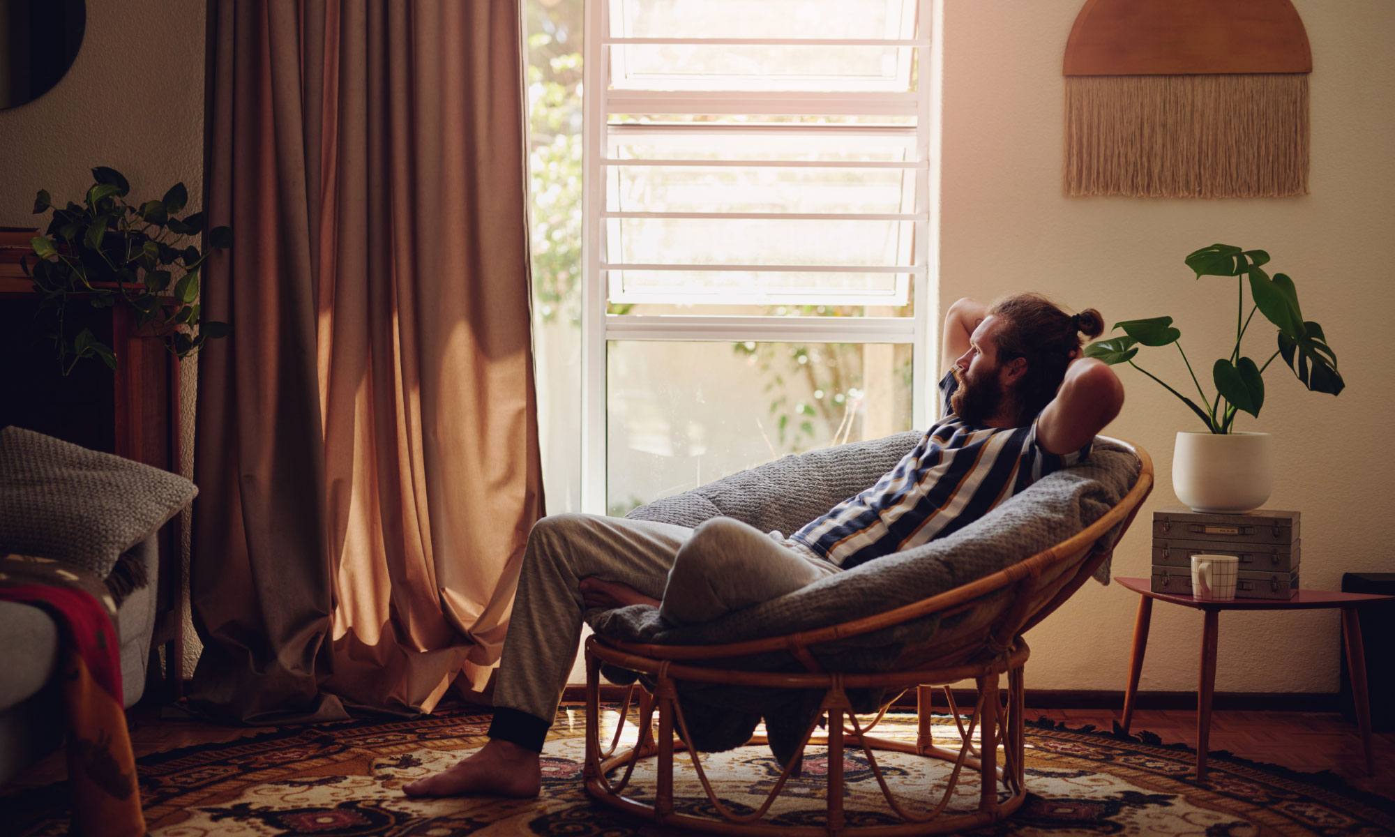Young adult man leaning back in a wicker chair while looking out his living room