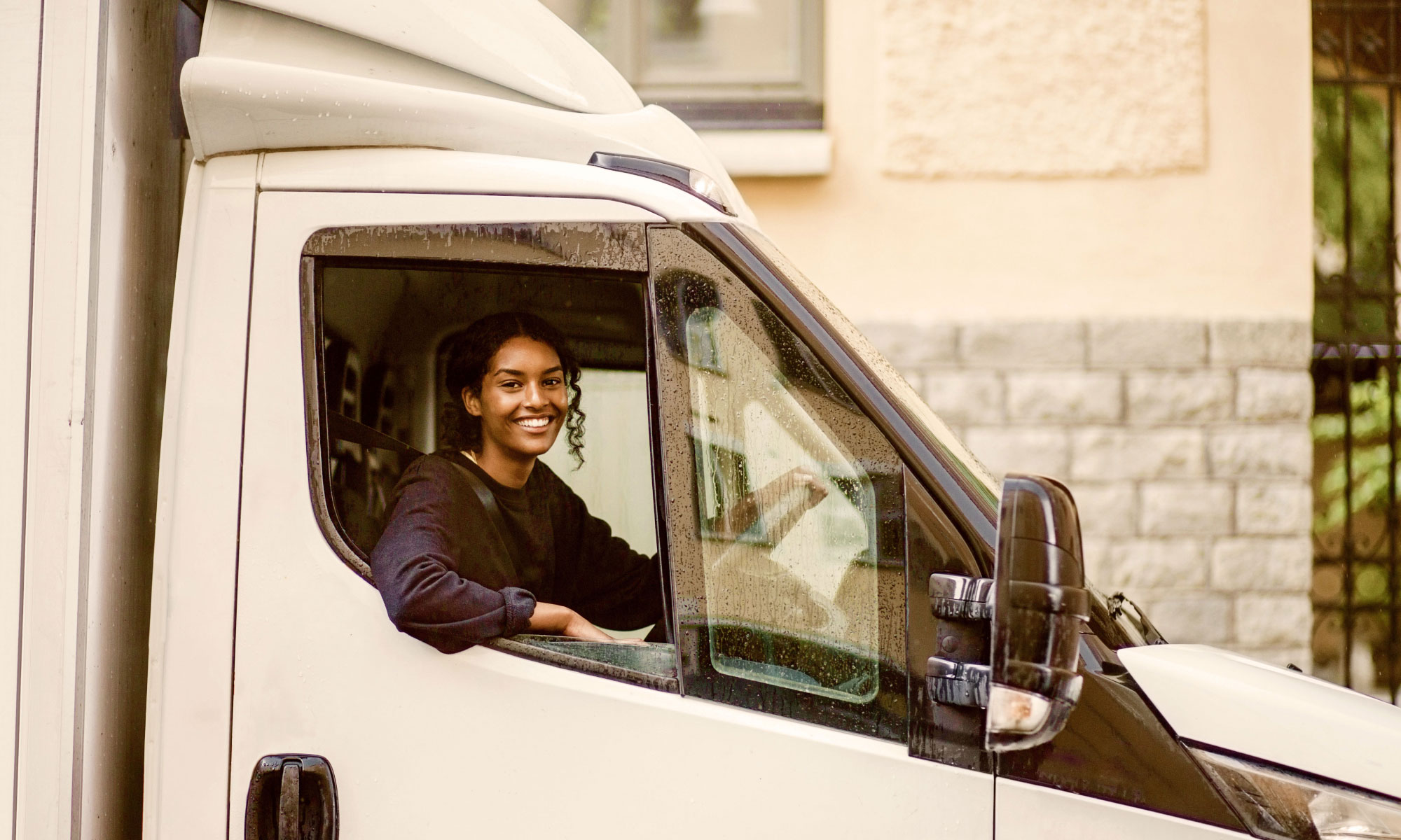 Young adult woman driving a white van and looking at the camera while smiling